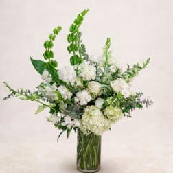 White floral arrangement in a clear glass vase with tall green spikes