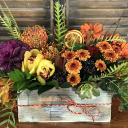 Autumn floral arrangement in a wooden box with orange, yellow, and purple blooms