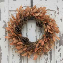 Autumn wreath with orange leaves, berries, and pinecones on a weathered white door