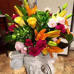Bright mixed bouquet with lilies, roses, and carnations in a white pedestal vase