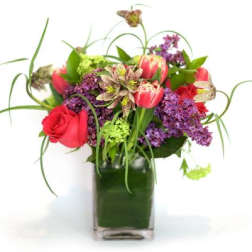Mixed bouquet of red roses and purple flowers in a square glass vase