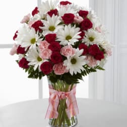 Bouquet of red roses, pink carnations, and white daisies in a glass vase