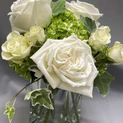 Small white rose and green hydrangea arrangement in a clear glass vase