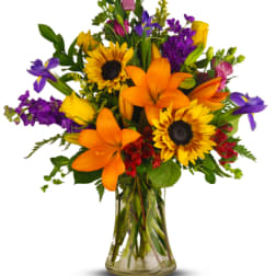 Colorful bouquet of lilies, sunflowers, and purple flowers in a glass vase