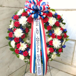 Standing floral wreath with red, white, and blue flowers and a memorial ribbon