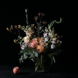 Peach and blush roses in a clear glass vase with airy greenery