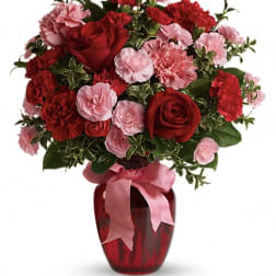 Red roses and pink carnations arranged in a red vase with a pink ribbon.