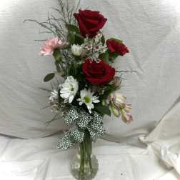 Red roses and mixed flowers in a clear glass vase with a patterned ribbon