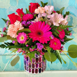 Mixed bouquet of pink and red flowers in a patterned vase
