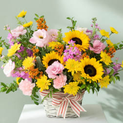 Basket arrangement with sunflowers, pink blooms, and a striped ribbon