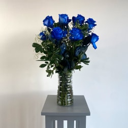 Blue roses in a clear glass vase with greenery