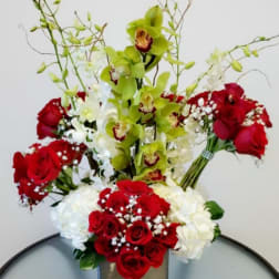 Tall arrangement of red roses, white blooms, and green orchids in a square vase