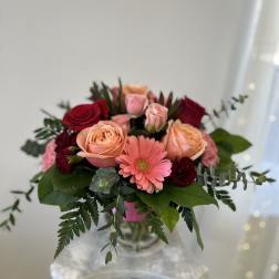 Bouquet of peach and red roses with a pink gerbera daisy in a glass vase