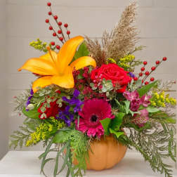 Colorful floral arrangement in a pumpkin-shaped container with a yellow lily and pink gerbera