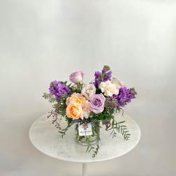 Mixed bouquet of pastel roses and purple flowers in a glass vase