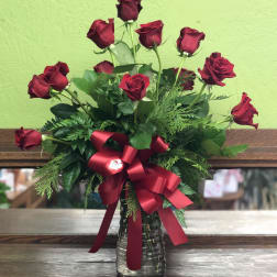 Arrangement of long-stemmed red roses in a clear glass vase with a large red bow.