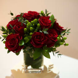 Red roses arranged in a clear glass vase with green berries