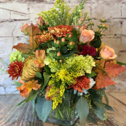 Autumn bouquet with orange and yellow flowers in a clear glass vase