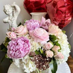 Pink and white flower arrangement in a glass vase with red heart balloons