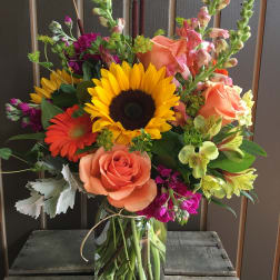 Mixed bouquet with sunflowers, roses, and snapdragons in a glass vase