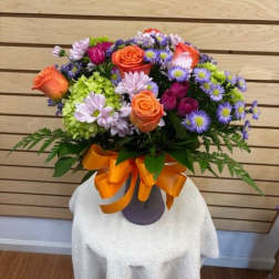 Bouquet of orange roses and purple daisies in a vase with an orange ribbon