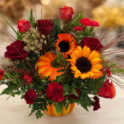 Autumn floral arrangement in a pumpkin container with sunflowers and red roses