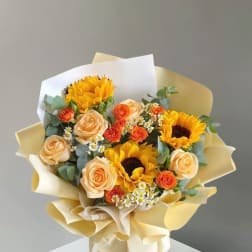 Bouquet of sunflowers, peach roses, and orange spray roses wrapped in cream paper