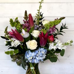 Mixed bouquet in a glass vase with pink lilies, white roses, and blue hydrangeas