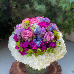 Round bouquet of pink roses, hydrangeas, and purple flowers in a glass vase