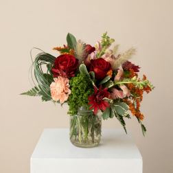 Mixed bouquet of red, pink, and orange flowers in a glass jar vase