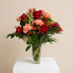 Mixed bouquet of red roses and peach carnations in a clear glass vase