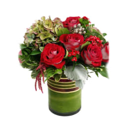 Red roses and mixed greenery in a green glass vase
