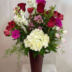 Mixed bouquet of red roses, white hydrangea, and pink flowers in a tall vase