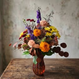 Mixed bouquet in an amber glass vase with purple, yellow, orange, and pink flowers