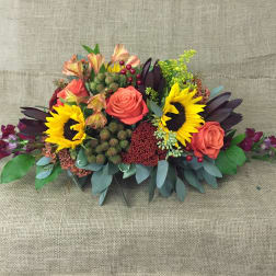 Low floral arrangement with sunflowers and coral roses on a burlap background