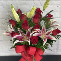 Bouquet of red roses and pink lilies in a glass vase with a red ribbon