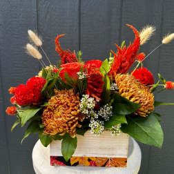 Red and orange floral arrangement in a wooden box with green leaves