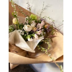 Hand-tied bouquet of pale pink and white flowers wrapped in kraft paper