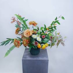 Mixed floral arrangement in a dark vase with peach roses and orange chrysanthemums