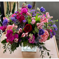 Mixed bouquet of pink, purple, and red flowers in a clear glass vase