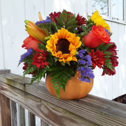 Bright mixed bouquet with a sunflower, roses, lilies, and purple filler in an orange vase