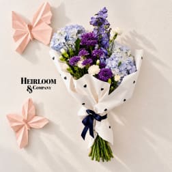Bouquet of purple, blue, and white flowers wrapped in white paper with black hearts