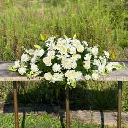 Long all-white arrangement of lilies, roses, and mums on a rustic wooden table outdoors