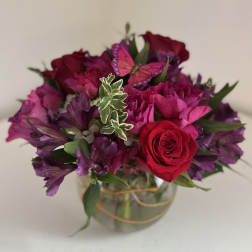 Bouquet of red roses and purple flowers in a glass vase with a butterfly decoration