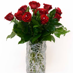 Red roses arranged in a clear glass vase with a silver wire wrap