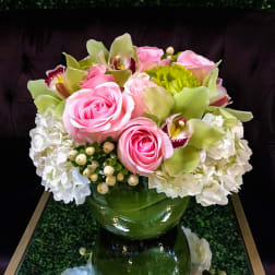Pink roses and green orchids arranged in a glass vase with white hydrangeas