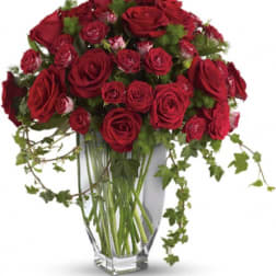 Red roses arranged in a clear glass vase with trailing ivy