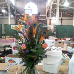 Tall tropical bouquet with orange bird-of-paradise and peacock feathers in a glass vase