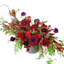 Red and burgundy floral arrangement in a gray vase