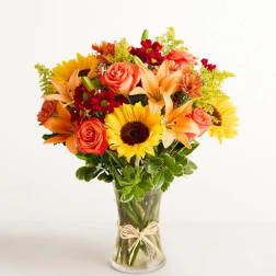 Bouquet of sunflowers, roses, and lilies in a clear glass vase